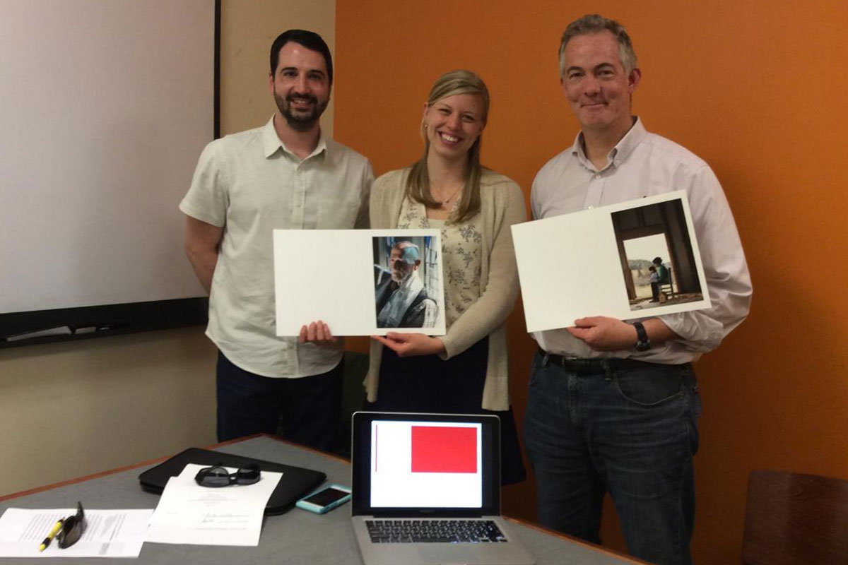 Three individuals holding printed project boards in a classroom setting.