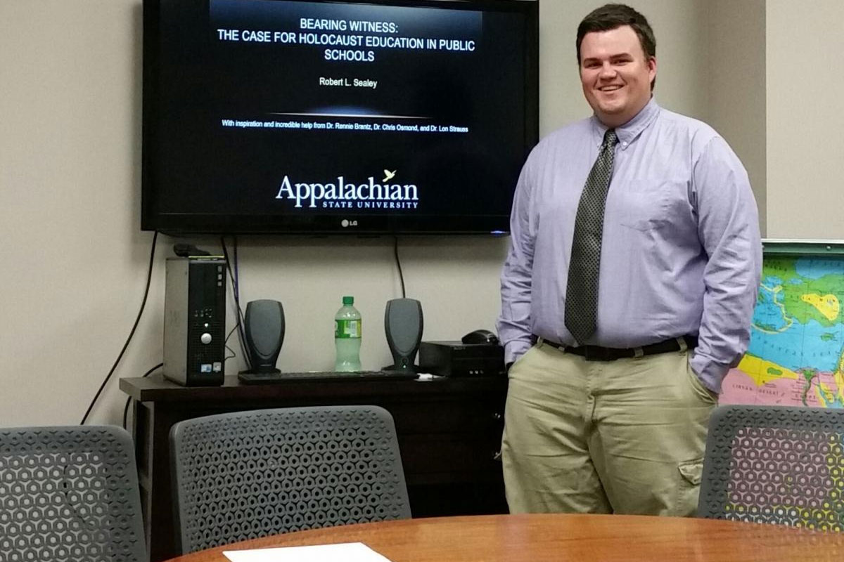 Individual standing beside a screen displaying a thesis presentation.