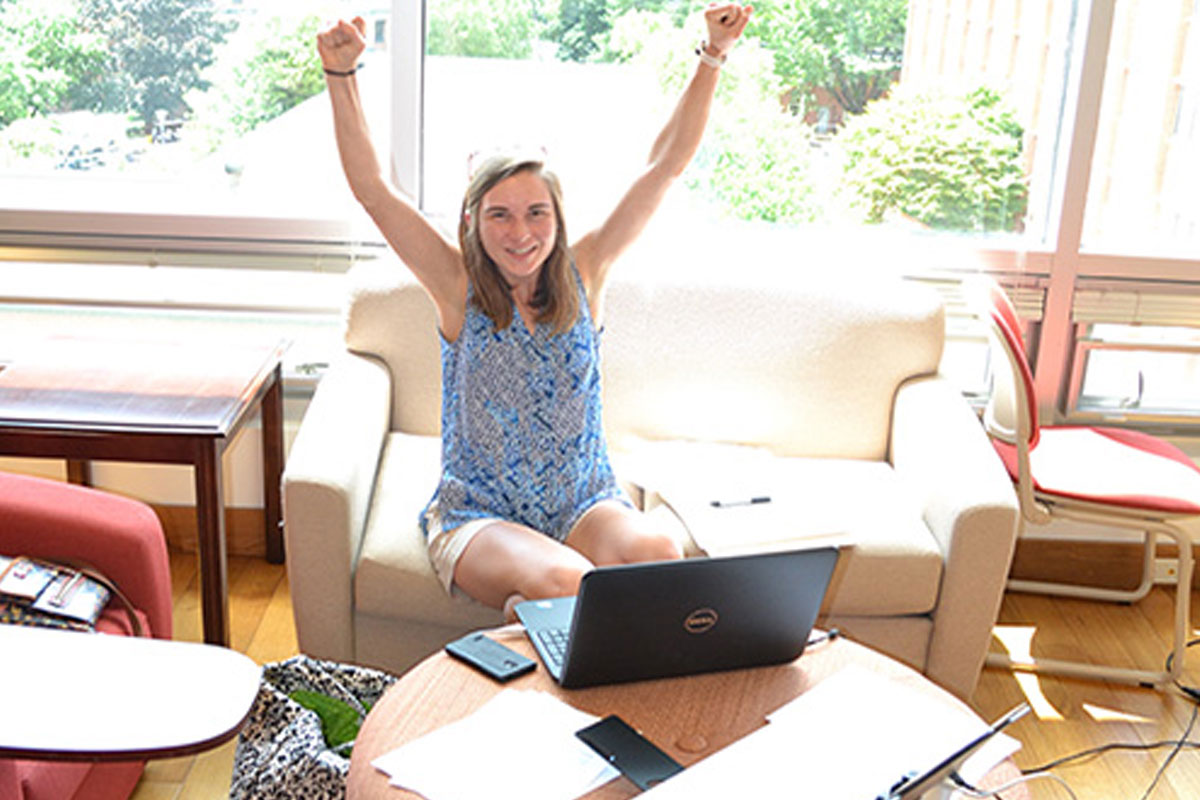 Person raising arms while sitting with a laptop in a bright room.