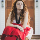Sophia White, a first-year Honors student at Appalachian State University, sits outside holding a red graduation cap and gown while looking upward.