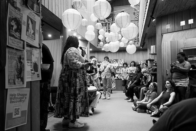 Ryan Stukes giving her thesis presentation to audience at The Happy Persimmon, April 2025. 